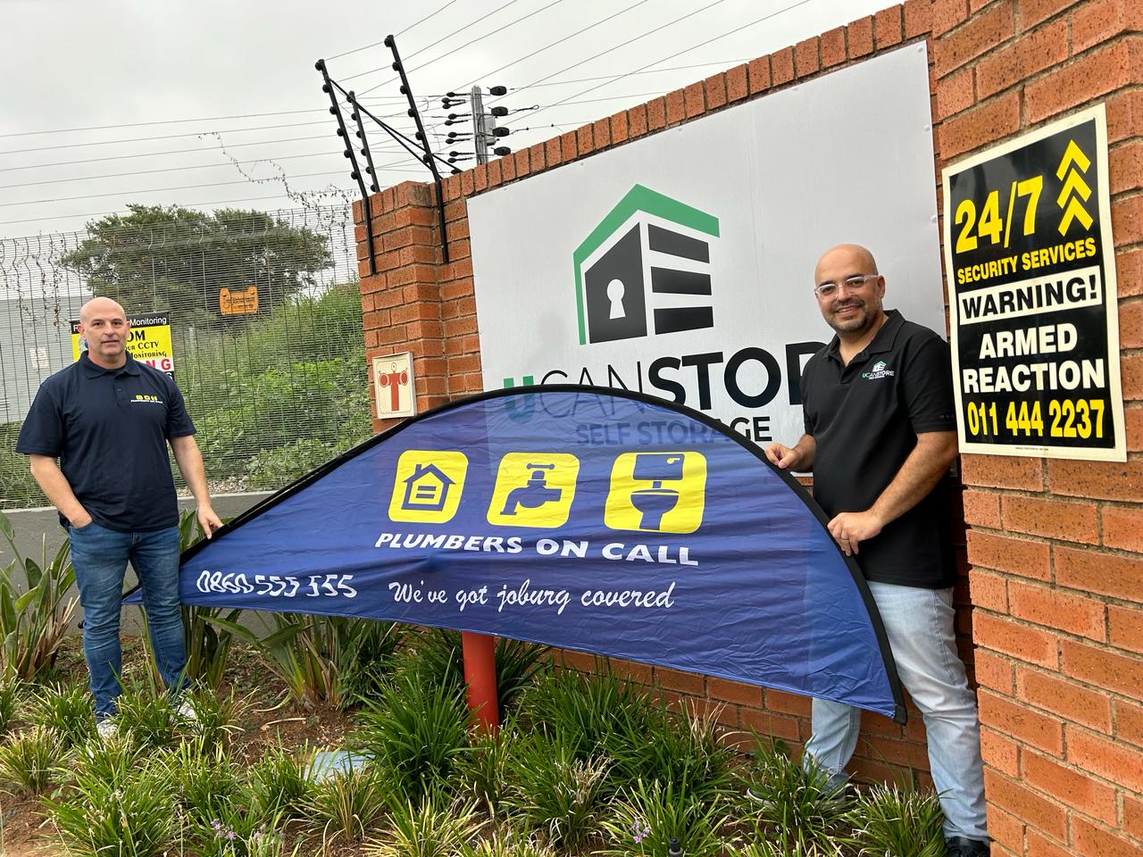 Two men with the plumbers on call signage standing in front of U can store branch 
